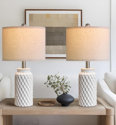 A pair of white textured ceramic table lamps with linen shades on a wooden console table.