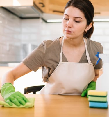 a woman in a apron and gloves cleaning a counter