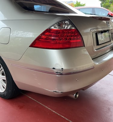 Rear bumper damage with paint scuffs and scratches on a silver sedan parked on a red driveway.