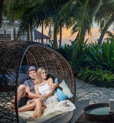 A romantic couple sitting in a cozy, woven wicker pod under tropical palm trees, enjoying