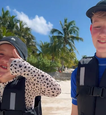 two boys in life jackets standing in the sand