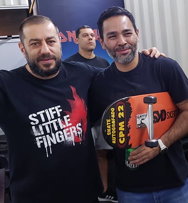 O vocalista da Banda CPM 22 em pé ao lado do ganhador, segurando o skates que ganhou da banda