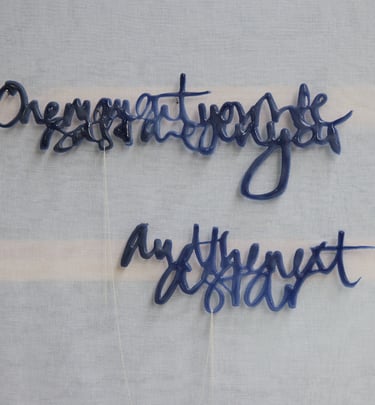 A glass sculpture with semi-abstract text hangs on a wall. its 2 sections are joined by silver chain