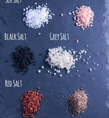 Assorted gourmet salts on a sheet: pink, black, red, and varieties on Cool Steel Blue background