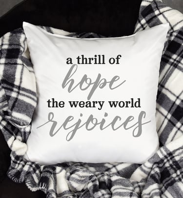 A throw pillow on a black & white checked throw over a black chair. Pillow reads, "A thrill of Hope the weary world Rejoices.