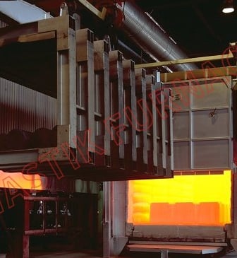 Industrial heat treatment furnace with open door showing glowing orange interior and loading mechanism.