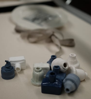 A group of small porcelain ink bottles,, in white and blue, are tumbled together in a display case