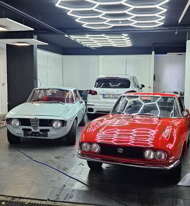 Zwei klassische Sportwagen (rot und weiß) in einer Werkstatt oder Ausstellungshalle.