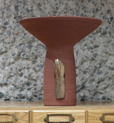 Tall ceramic vessel in deep red stoneware, with a bronze sculpted hand mounted on the base.