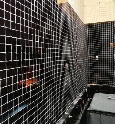 Close-up of a sturdy safety net installed on a balcony overlooking a green courtyard.