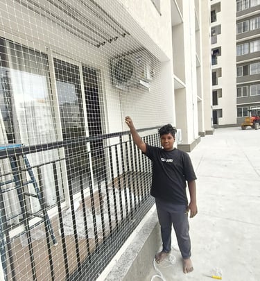 View from inside a balcony protected by a fine mesh safety net, with plants and furniture visible.