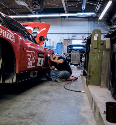 A mechanic performs professional maintenance on a red Ferrari race car in an automotive repair shop.