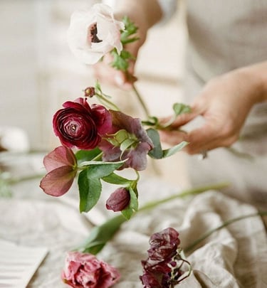 Florista sosteniendo una rosa roja sobre mesa de lino claro.