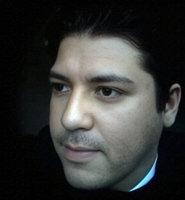 Close-up portrait of a dark-haired man looking sideways against a dark background.