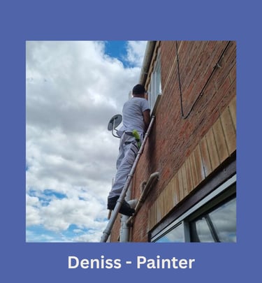 Portrait of Deniss, an LPAD painter, on a ladder painting the exterior of an upper window.