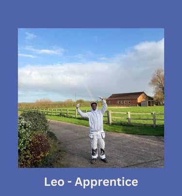 Portrait of Leo, an apprentice painter, standing on a driveway and gesturing towards a rainbow.