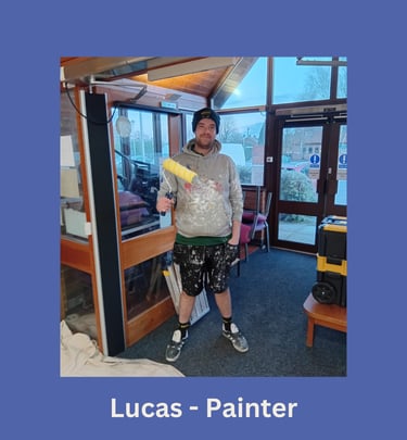 Portrait of Lucas, an LPAD painter, standing and holding a roller whilst smiling at the camera.