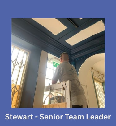 Portrait of Stewart, a senior team leader, on a ladder painting a doorway and facing away.