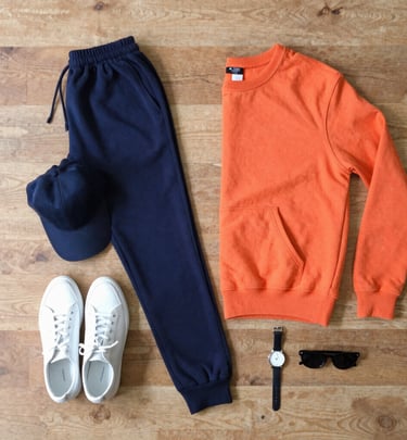Flat lay of crew & co sweatpants, a sweatshirt, and a hat arranged on a wooden surface.