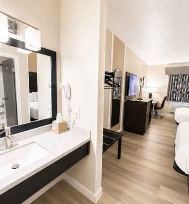 Modern hotel room with two queen beds, a vanity sink, and a flat-screen TV.