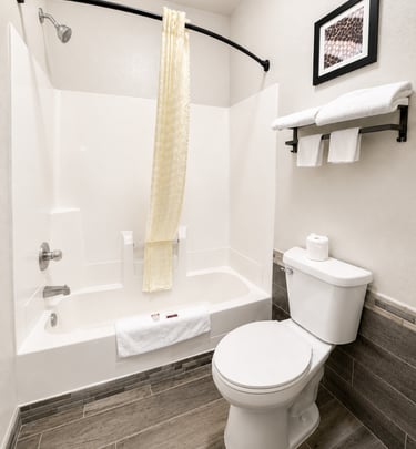 Modern bathroom interior featuring a white bathtub, toilet, and grey wood-look tile floors.