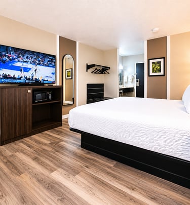 Modern hotel room with king bed, flat-screen TV, wood flooring, and ironing station.