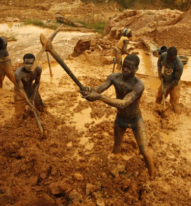 Artisanal gold miners using pickaxes and shovels to excavate muddy soil at an open-pit mine site.