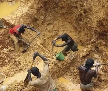 Artisanal gold miners using manual tools and shovels to dig in a muddy open-pit mine.