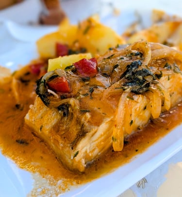 Close-up of cod cooked in a tomato, onion, and pepper sauce.