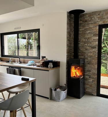 Poêle à bois moderne installé dans une cuisine contemporaine avec mur en pierre et baies vitrées