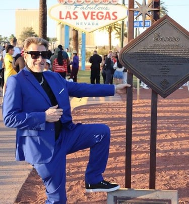 Tim in a blue suit poses by a bronze plaque near the Welcome to Fabulous Las Vegas sign.