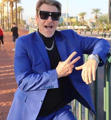 Tim in a vibrant blue suit and oversized sunglasses posing with a peace sign outdoors.