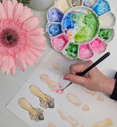 Hand painting watercolor shoes with palette and pink flower in background.