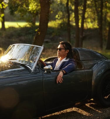 A photo of a man sitting in a 1958 MG MGA Roadster at sunset