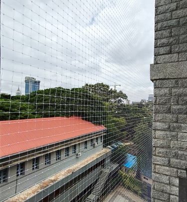 Technician carefully installing a pigeon net on a balcony railing under bright daylight
