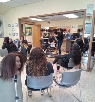 Students in a cosmetology classroom practicing hair styling on mannequins and models.