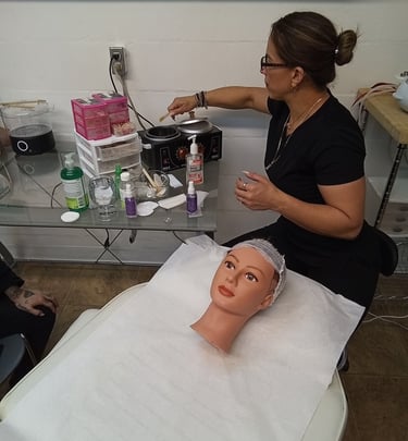 Esthetician student practicing facial waxing techniques in a college beauty salon training setting.