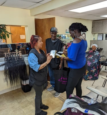Student hair stylists discussing products and extensions with a teacher inside beauty school.