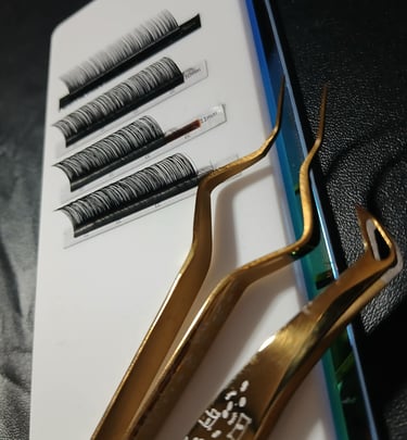 Professional gold lash tweezers next to a tray of individual eyelash extensions for lash artists.