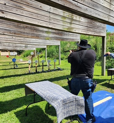 A cowboy action shooter aims a shotgun at steel targets on an outdoor shooting range.