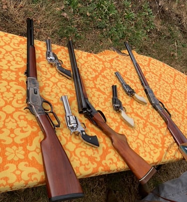 Collection of Western-style firearms including lever-action rifles, revolvers, and a double-barrel shotgun on a blanket.