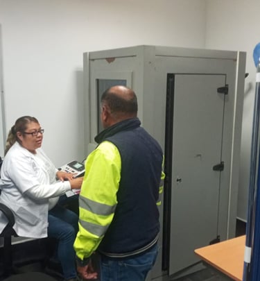 Paciente realizando una prueba de audiometría en una cabina especializada, acompañado por un profesi