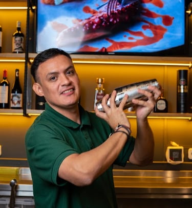 Camarero preparando cóctel en barra de restaurante, ambiente acogedor y profesional.