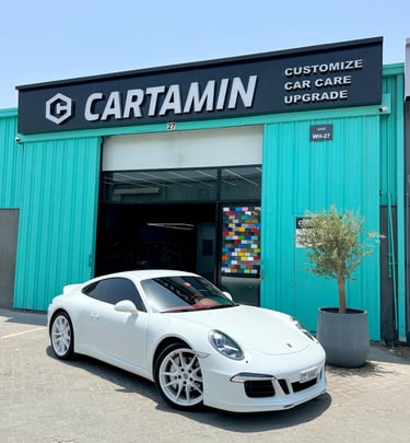 A white Porsche sports car parked outside Cartamin car care and customization shop.