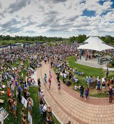A large crowd gathers for a political rally and protest at Caras Park with a white tent stage.