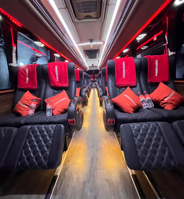 Luxury bus interior featuring reclining black leather seats with red pillows and ambient led lighting.