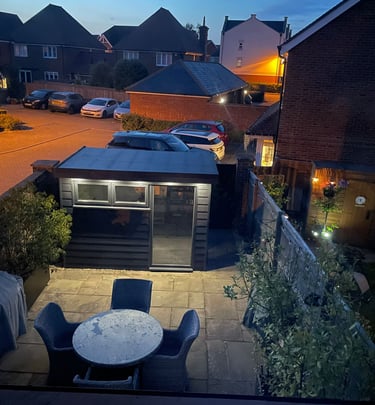 Backyard stone patio with a modern grey garden office and outdoor furniture at dusk.