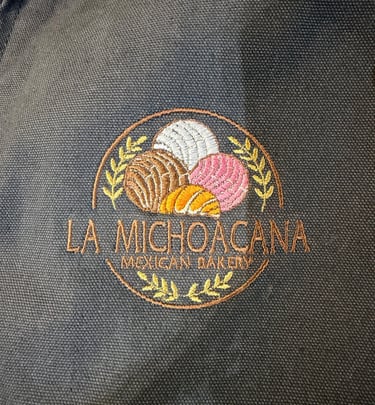 Embroidered logo for La Michoacana Mexican Bakery featuring colorful concha pastries on dark fabric.