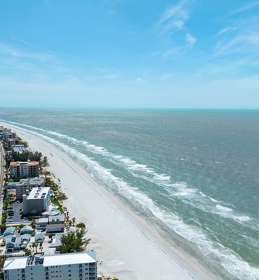 Aerial view of a white sand beach coastline with beachfront hotels and ocean waves.