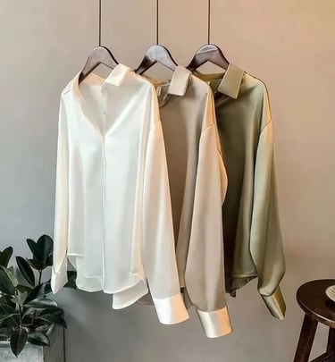 Elegant long-sleeve silk button-down blouses in white, beige, and olive green hanging on wooden hangers.